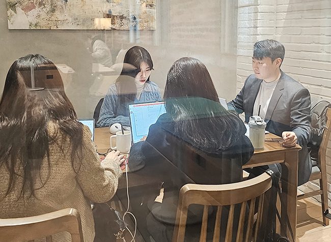 유리 너머로 보이는 플라톤마케팅 회의 장면. 네 사람이 노트북과 음료를 놓고 긴 시간 작업하고 있다
